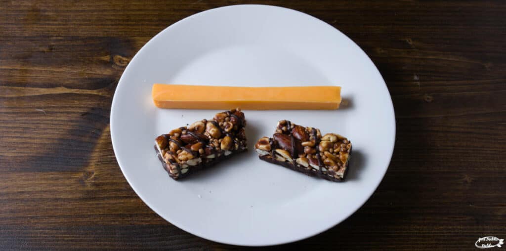 A plate with a snack containing a cheese stick and a granola bar.