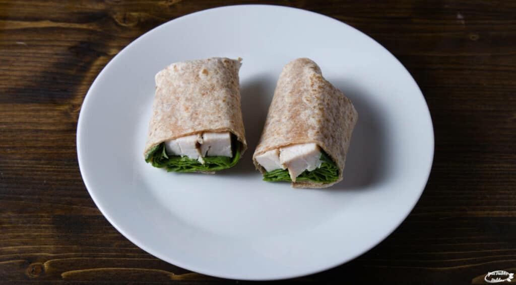 A plate with a chicken wrap containing chicken and spinach.