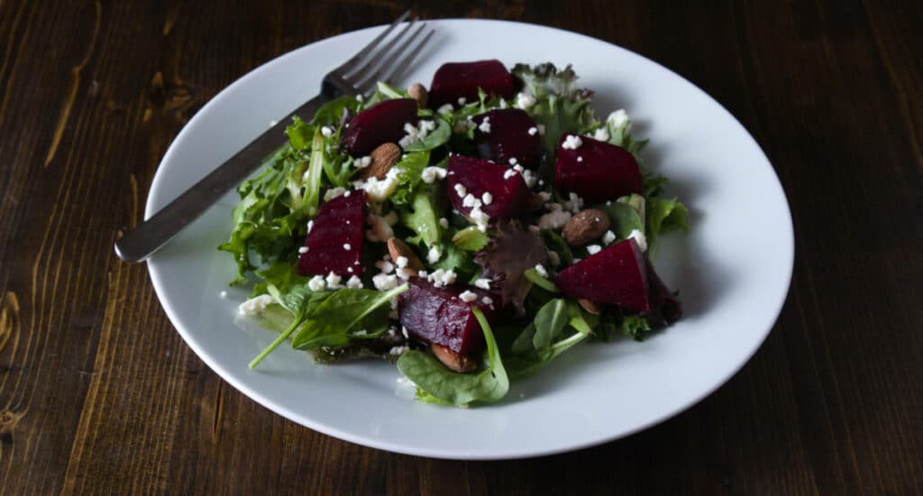 A beet salad consisting of beets, mixed greens, feta cheese, and almonds served on a plate