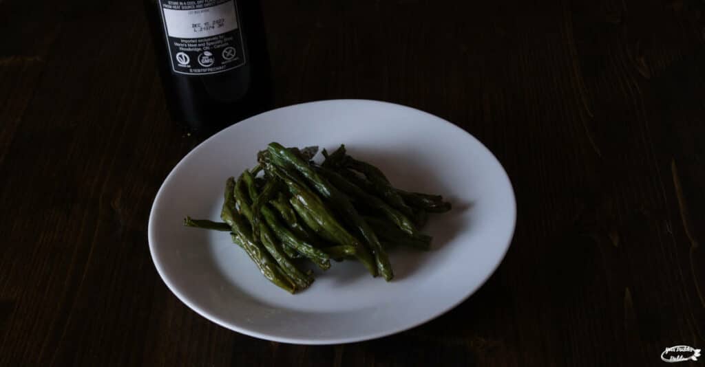 A plate of beans baked with a coating of olive oil and spices, with a bottle of olive oil behind it