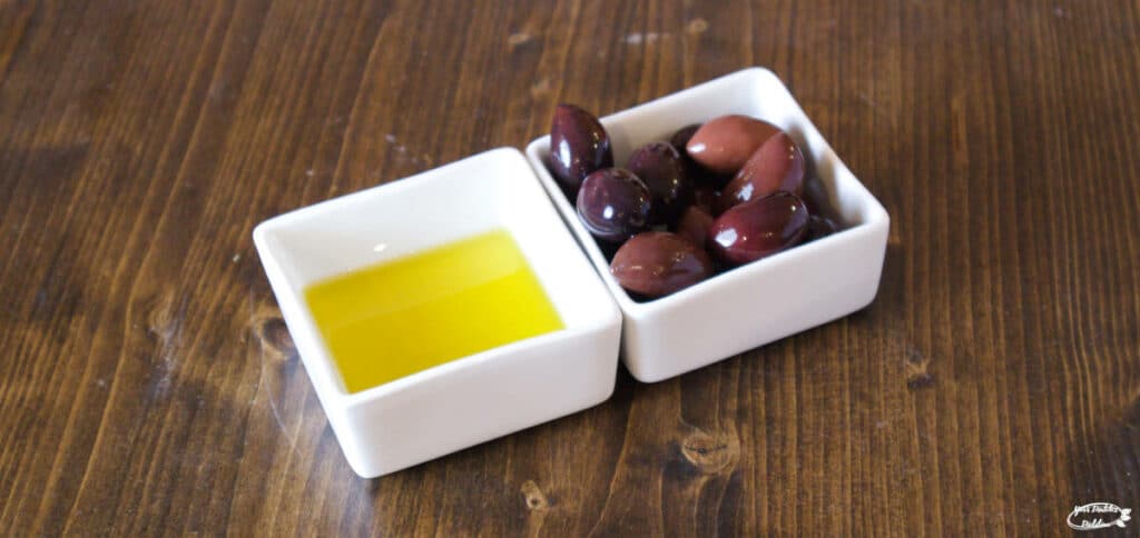 Two small dishes, one containing olives, the other containing olive oil