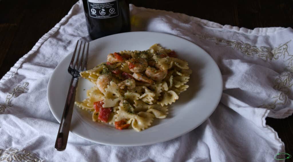 A plate of seafood pasta, with a sauce made of olive oil. This is set on a plate, on a white cloth placemate with a bottle of olive oil placed behind it.