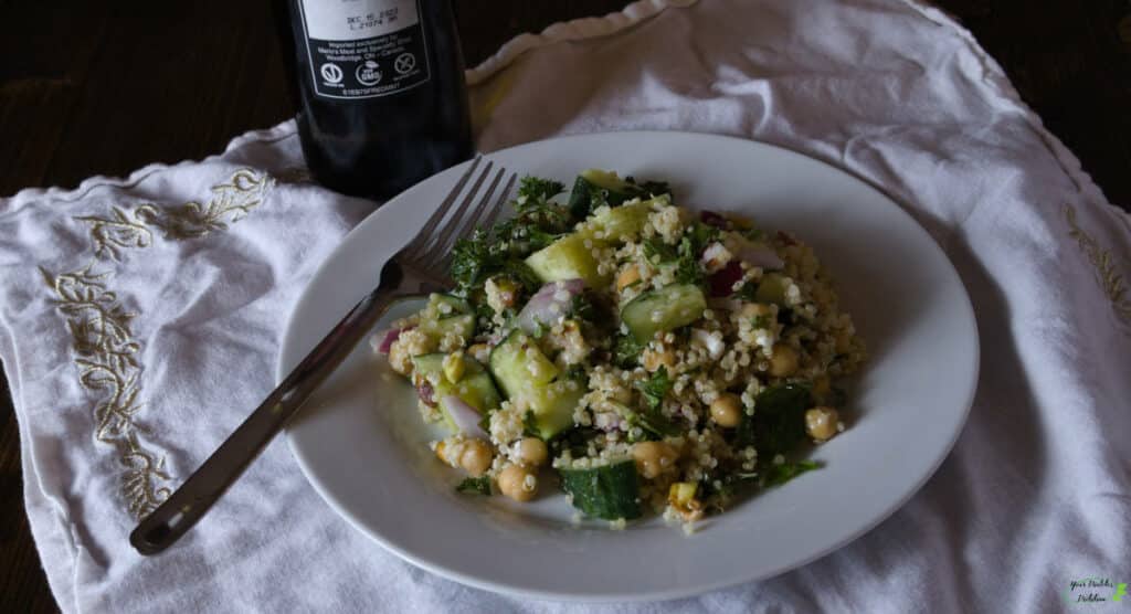 A bean salad with a fork on a plate, in front of a bottle of olive oil, set on top of a white place mat